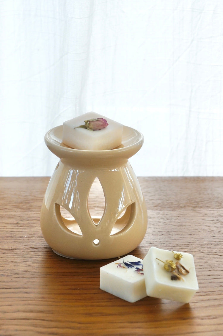 beige aromalampa med en doftpralin i. Två doftpraliner ligger på bordet snett framför aromalampan