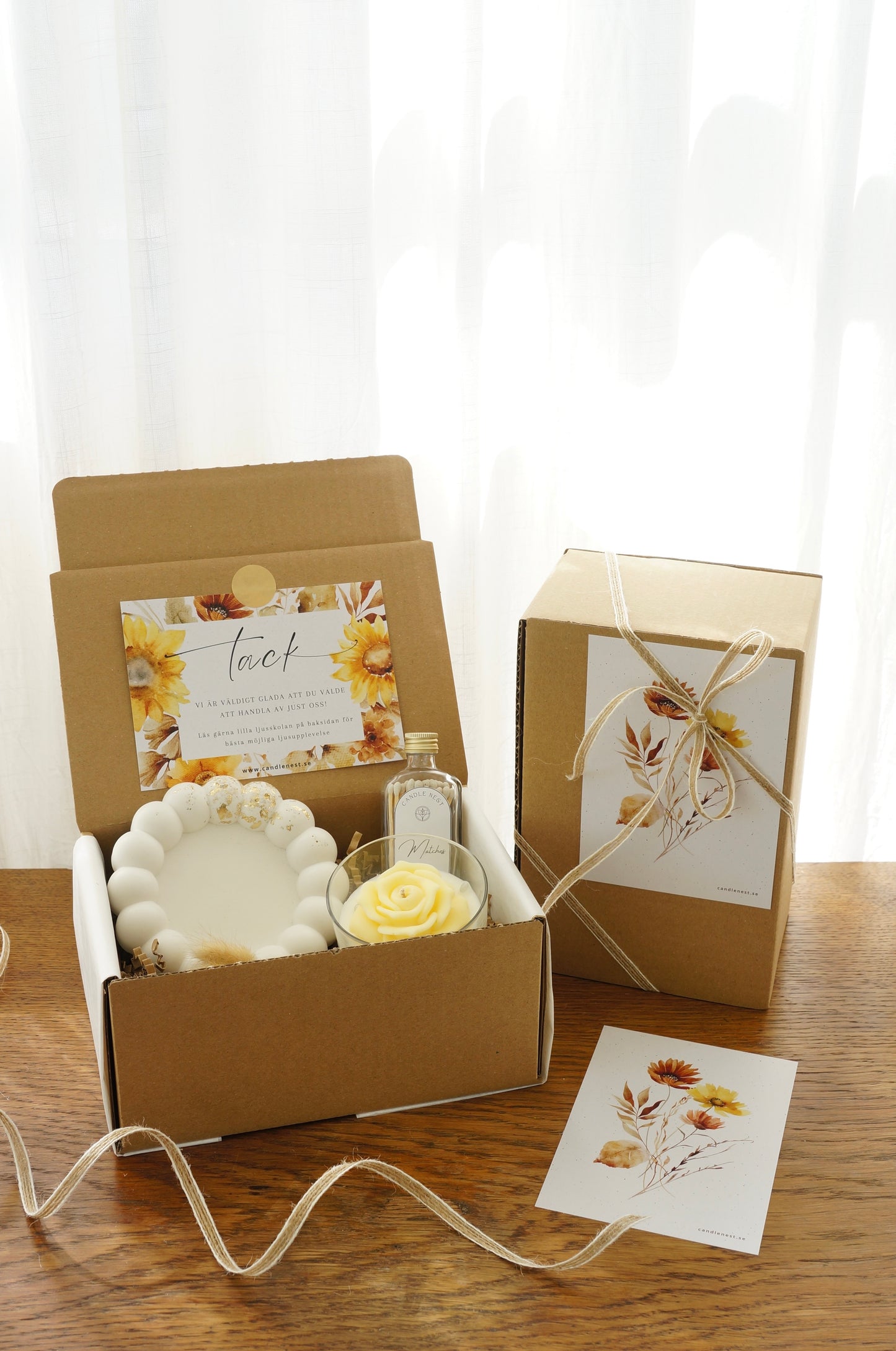 Lyxig Presentbox med ljusfat, Booms & Bubbles doftljus (Limoncello), flaska med tändstickor. Bild snett ovanifrån med en inslagen presentbox vid sidan.