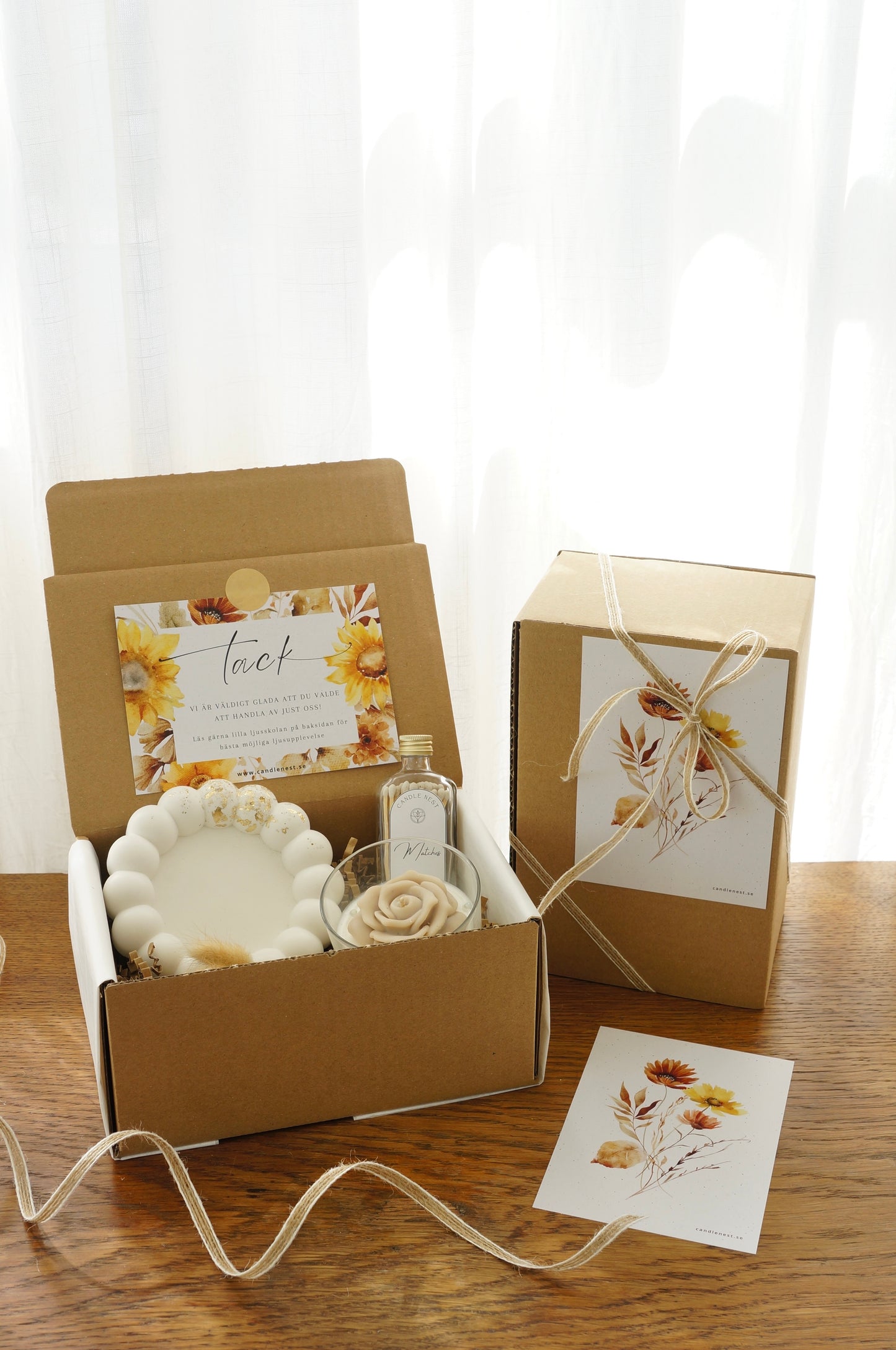 Lyxig Presentbox med ljusfat, Booms & Bubbles doftljus (Casablanca cocktail), flaska med tändstickor. Bild snett ovanifrån med en inslagen presentbox vid sidan