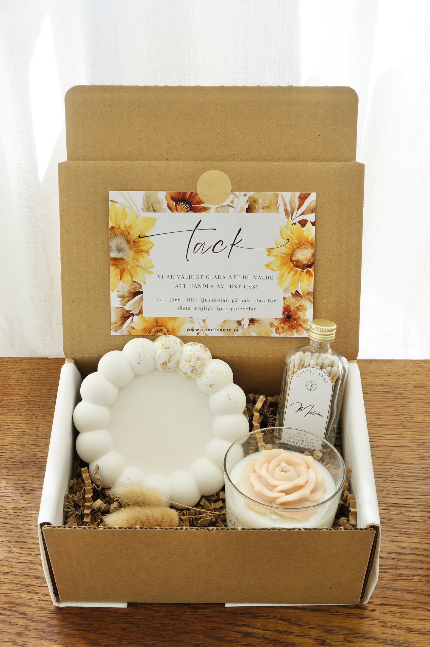 Lyxig Presentbox med ljusfat, Booms & Bubbles doftljus (Pomelo mimosa), flaska med tändstickor. Bild snett ovanifrån.