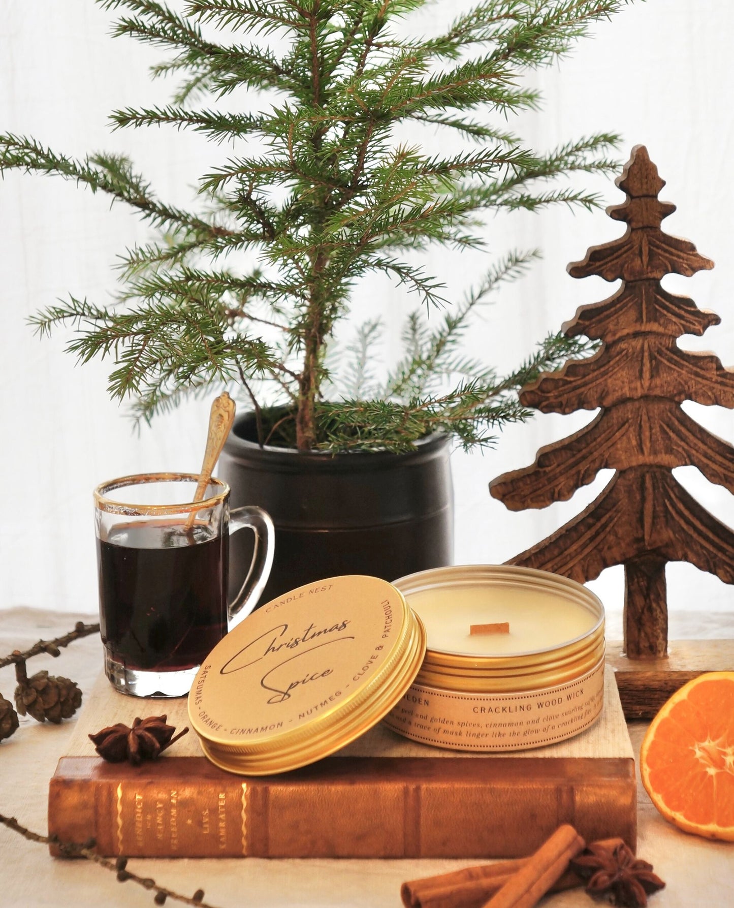 Ett doftljus i en guldig aluminiumburk står på en äldre bok med rygg av läder. Ljusets lock står lutat mot burken. På locket finns texten ” Christmas spice” skriven med snirklig text. Bakom ljuset syns en Grankvist i en urna. Vid sidan om Ljuset står en liten transparant kopp av glas med glögg i. Kanel, Stjärnanis och clementiner är utplacerade runt ljuset