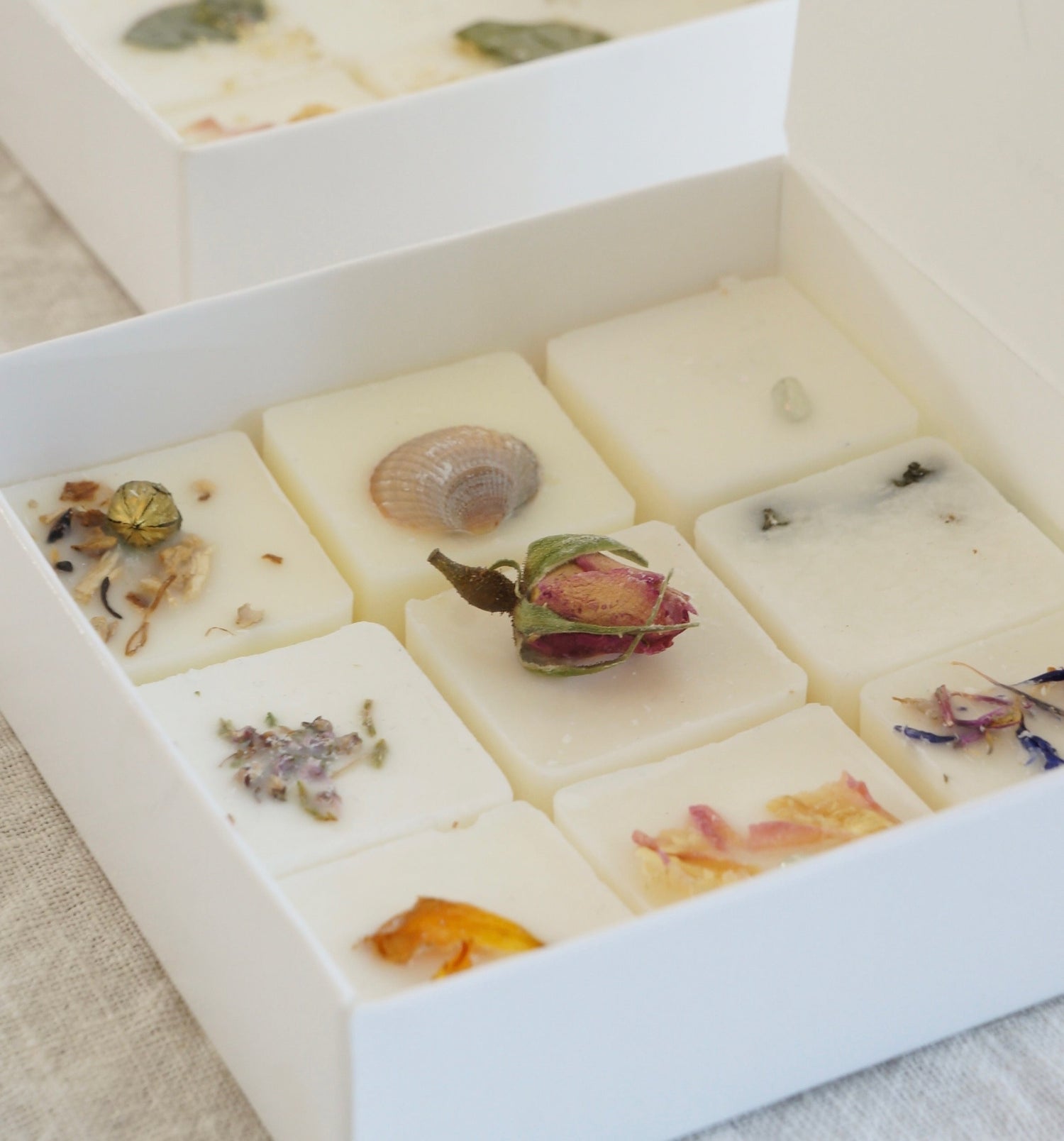 Öppen vit ask med nio olika doftpraliner i, alla med olika dekoration av torkade blommor
