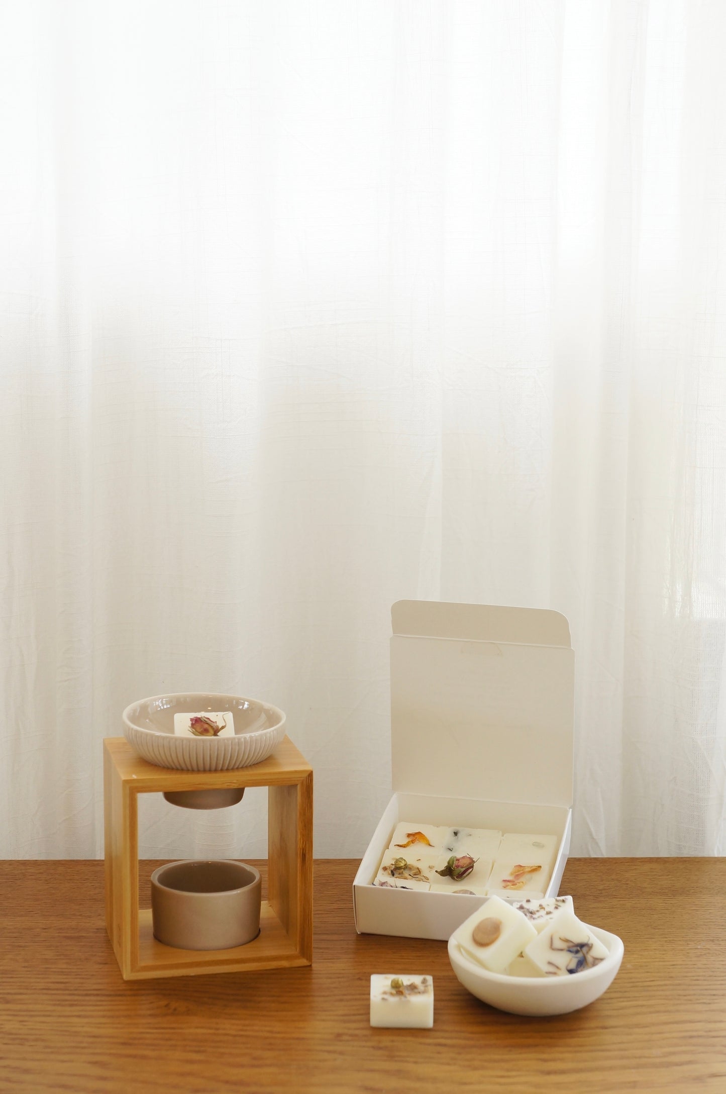 Modern och rustik aromalampa i beige keramik och bambu som står på ett bord av trä. Ask med doftpraliner finns på bilden samt en liten skål av gips med doftpraliner i