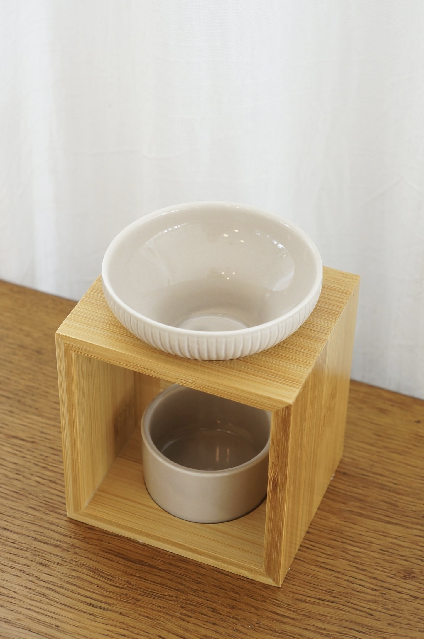 Modern och rustik aromalampa i beige keramik och bambu som står på ett bord av trä. Vit bakgrund. Bild tagen snett uppifrån