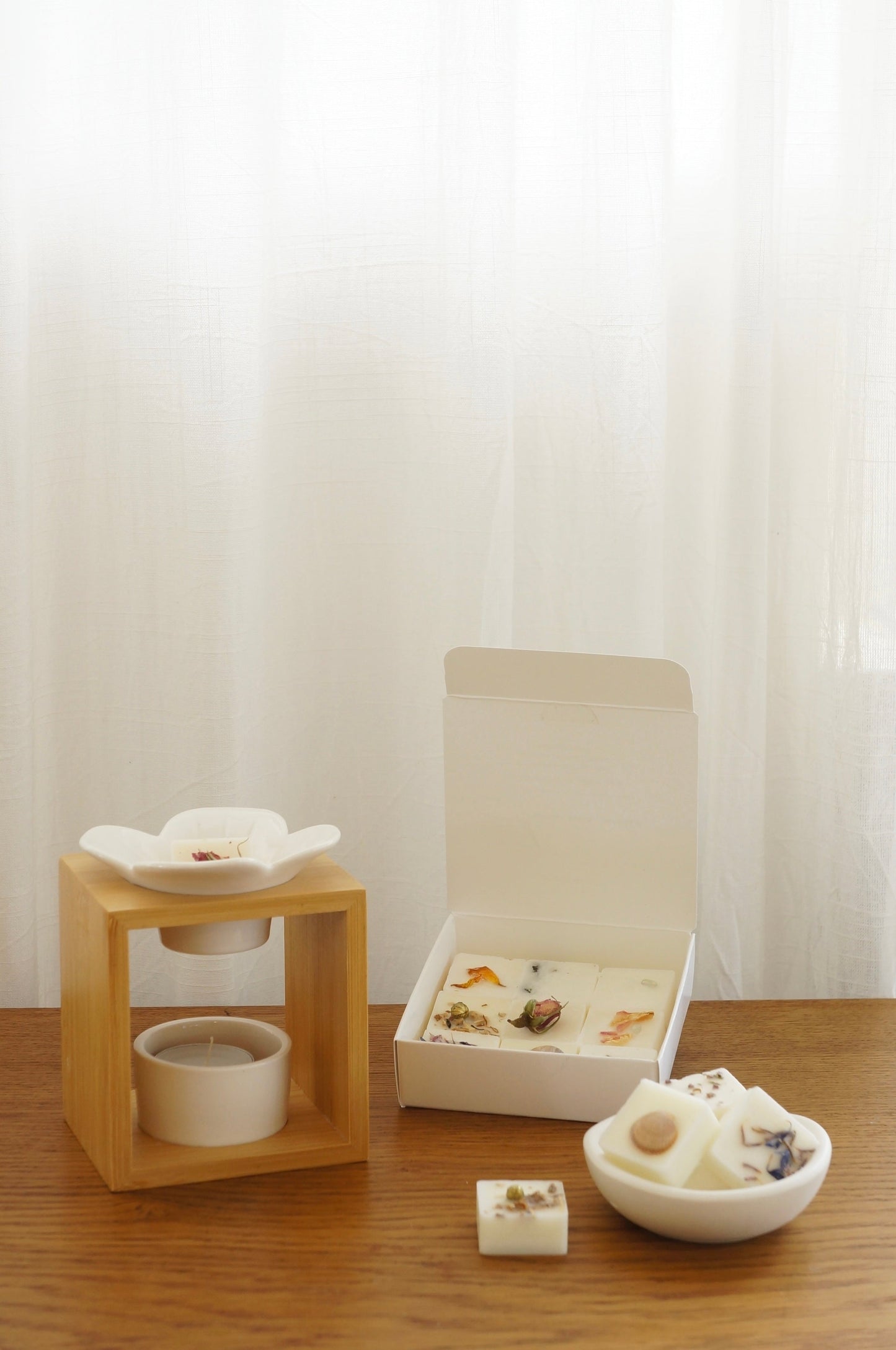 Modern och rustik aromalampa i vit keramik och bambu som står på ett bord av trä. Ask med doftpraliner finns på bilden samt en liten skål av gips med doftpraliner i