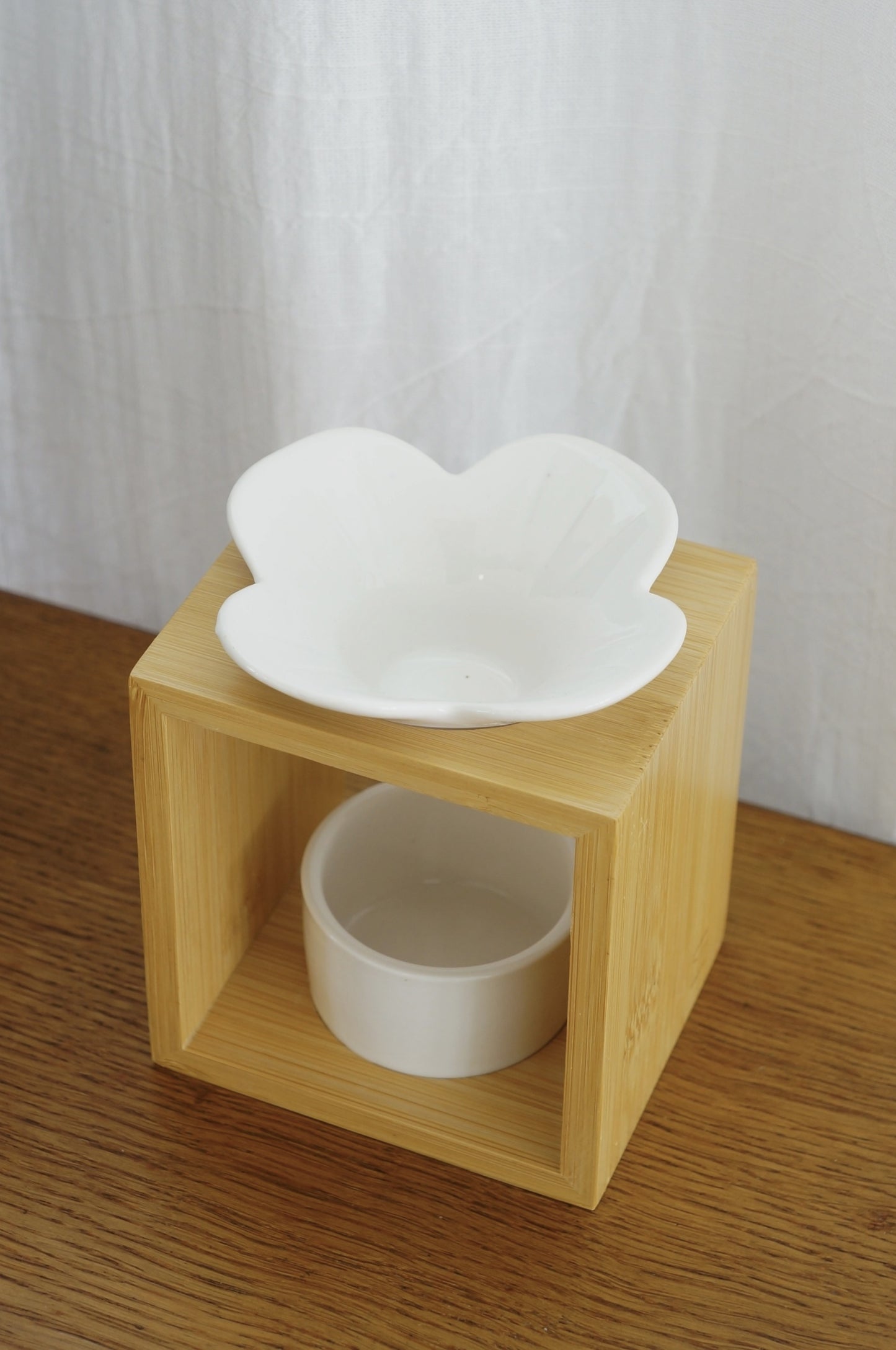 Modern och rustik aromalampa i vit keramik och bambu som står på ett bord av trä. Vit bakgrund. Bild tagen snett uppifrån