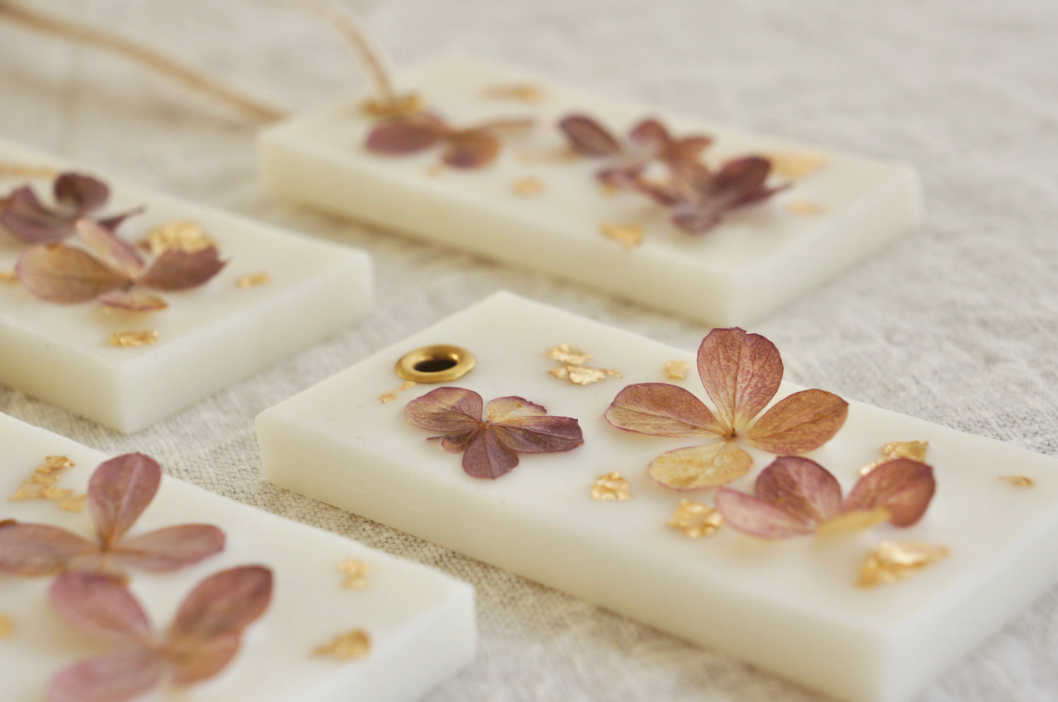Ett rektangulärt dofthänge dekorerat med torkad hortensia och bladguld. Flera stycken ligger på en vit duk