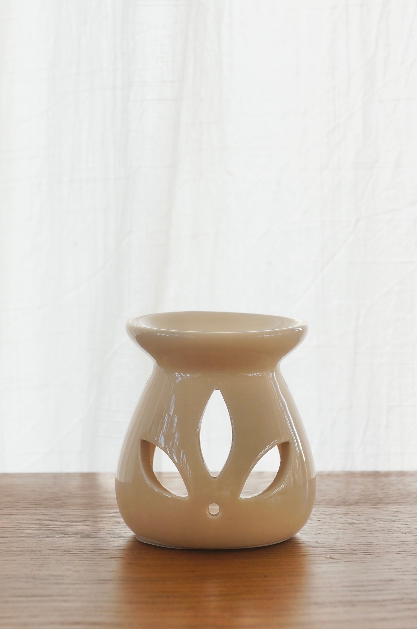Aromalampa i porslin. Beige. Bild tagen framifrån. Lampan står på ett bord av trä. Vit gardin i bakgrunden.