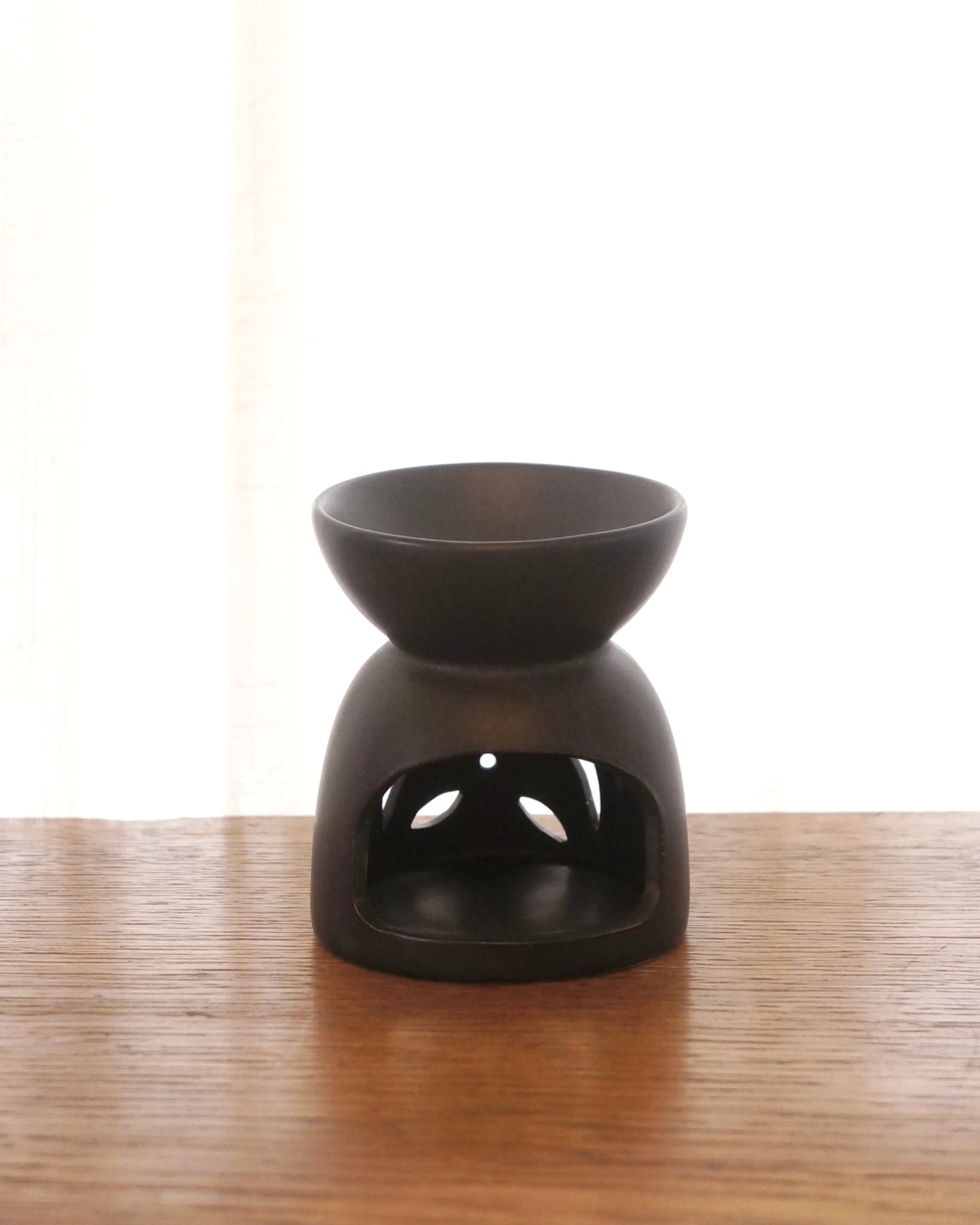En liten svart aromalampa i oval form står på ett bord av trä. Baksida.