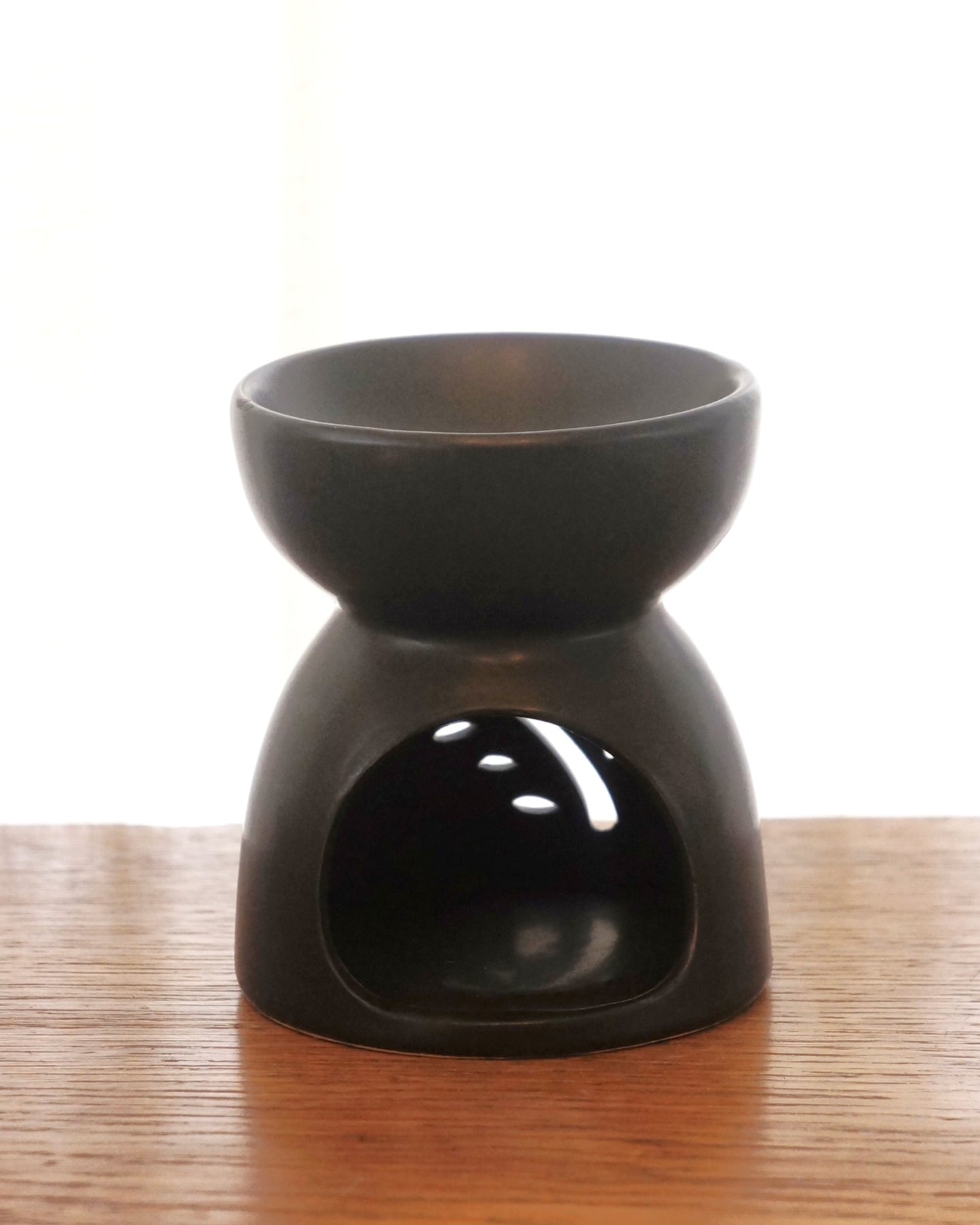 svart aromalampa i oval form står på ett bord av trä. Lampans baksida syns på bilden.