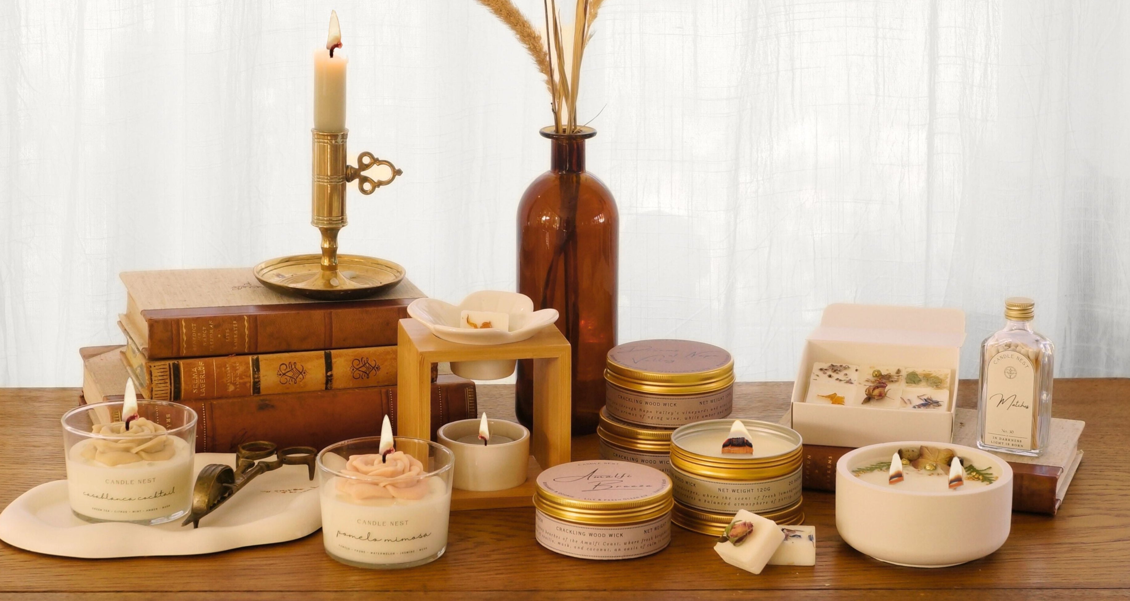 candle ensts hela produktutbud på en bild. Ljus, doftpraliner och aromalampor står på ett bord av mörkt trä. Ljusen är tända.