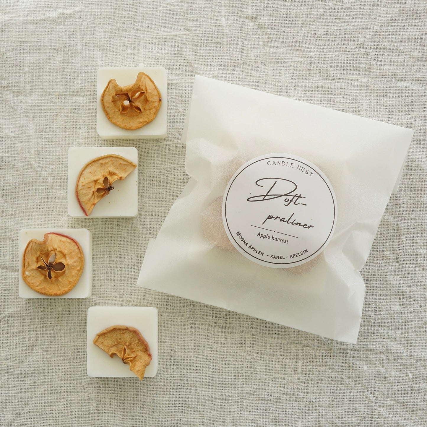 4 st doftpraliner i doften "Apple Harvest" och en påse med doftpraliner ligger på en vit linneduk. Doftvaxen är dekorerade med små torkade skivor av äpple.