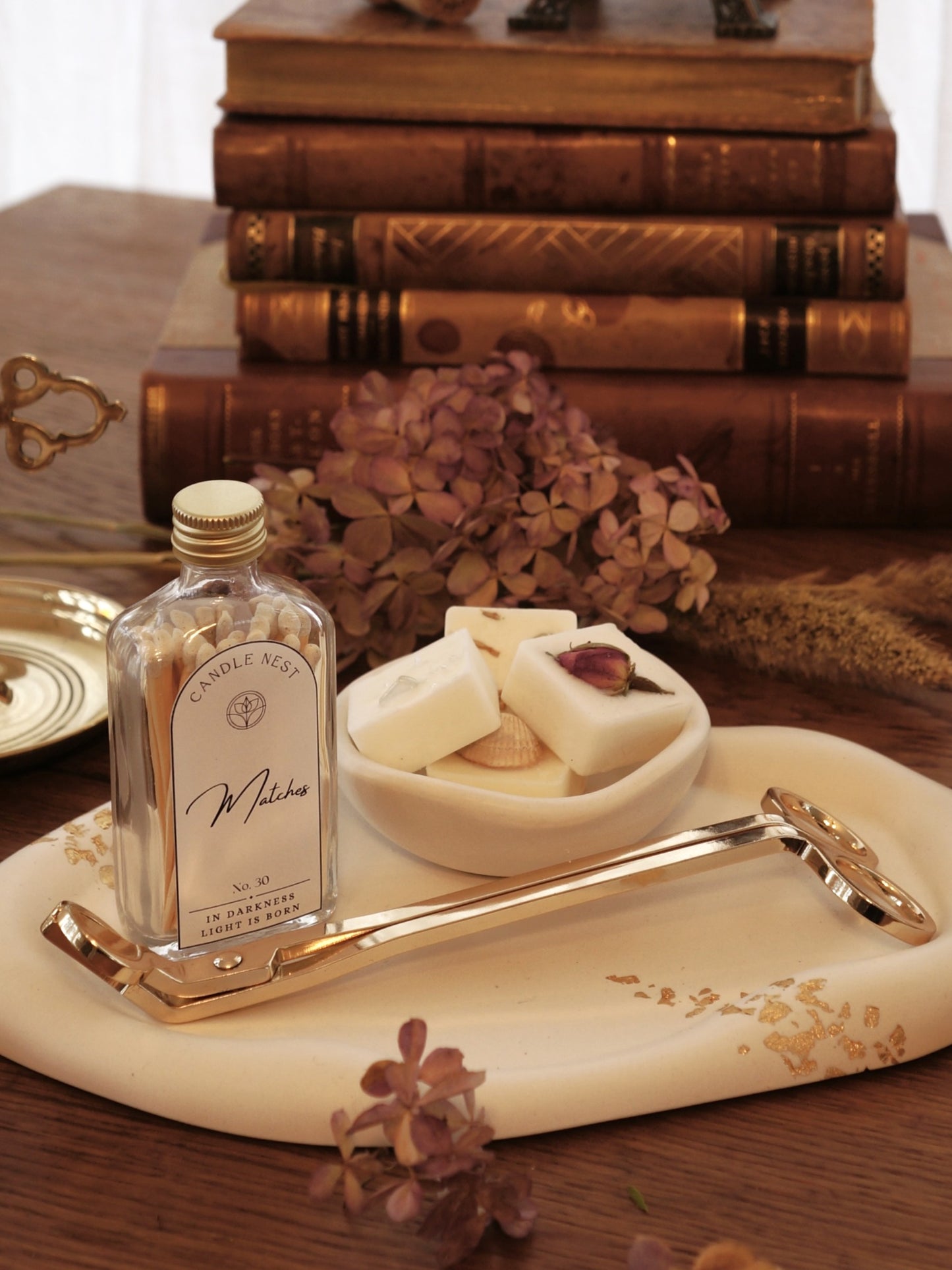 Ljusfat med guld dekor. På detta står en flaska med tändstickor, en skål med doftpraliner i och en vektång ligger på fatet