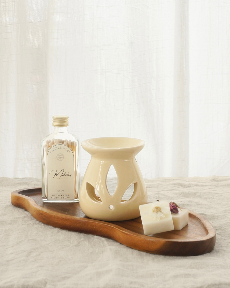 Avlångt fat i akaciaträ med rundade kanter, placerat på en ljus duk av linnetyg. På fatet står en aromlamapa, en flaska med tändstickor. Två doftvax ligger framför aromalampan på fatet.