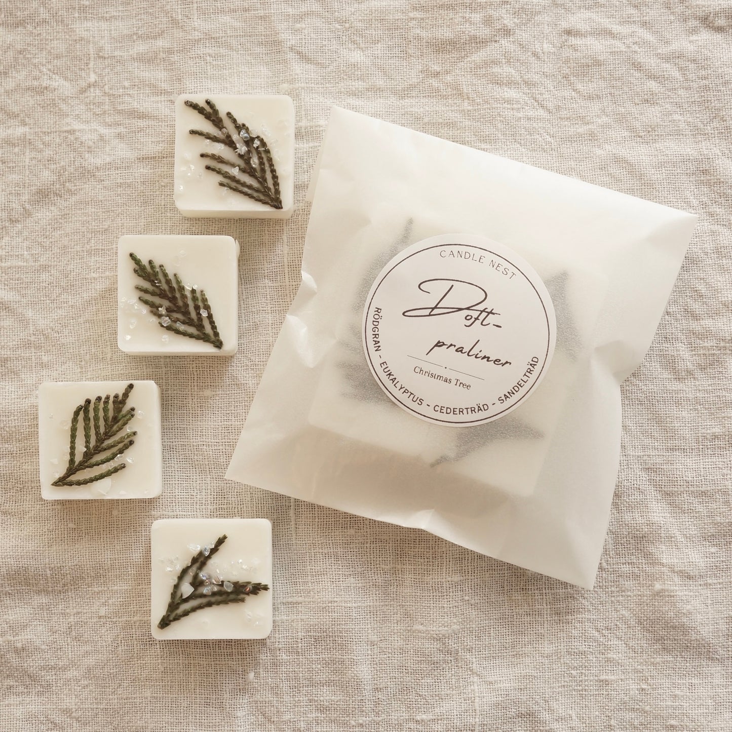 En vit halv halv transparent påse med doftpraliner i ligger på ett bord omgiven av fyra stycken doft praliner dekorerade med grankvistar