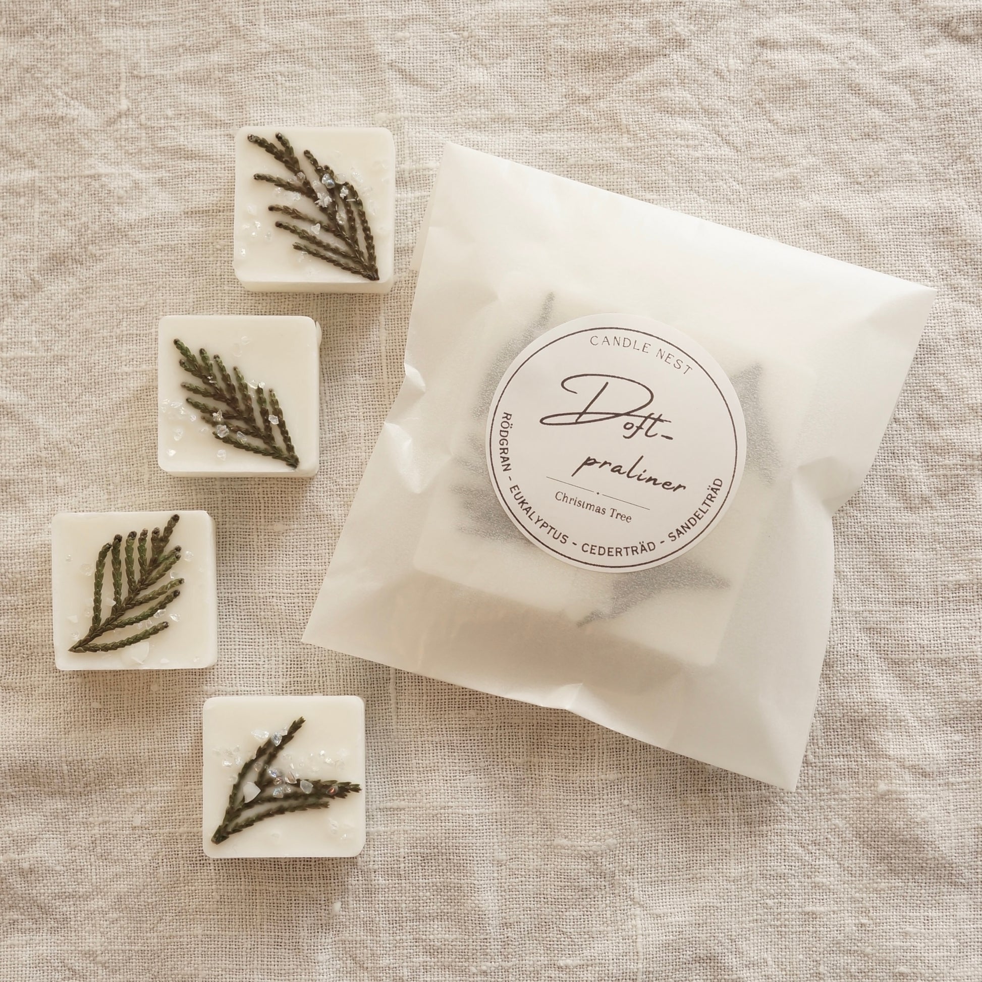 En vit halv halv transparent påse med doftpraliner i ligger på ett bord omgiven av fyra stycken doft praliner dekorerade med grankvistar