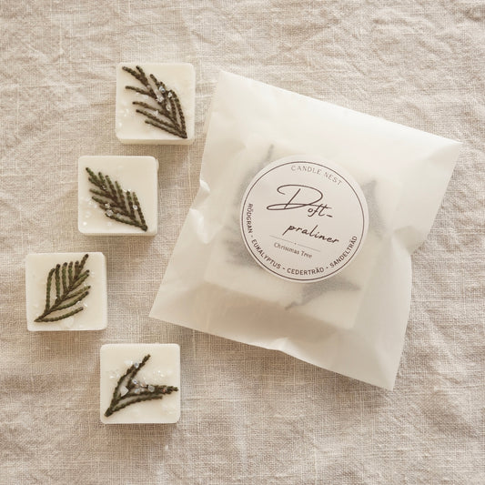 En vit halv halv transparent påse med doftpraliner i ligger på ett bord omgiven av fyra stycken doft praliner dekorerade med grankvistar