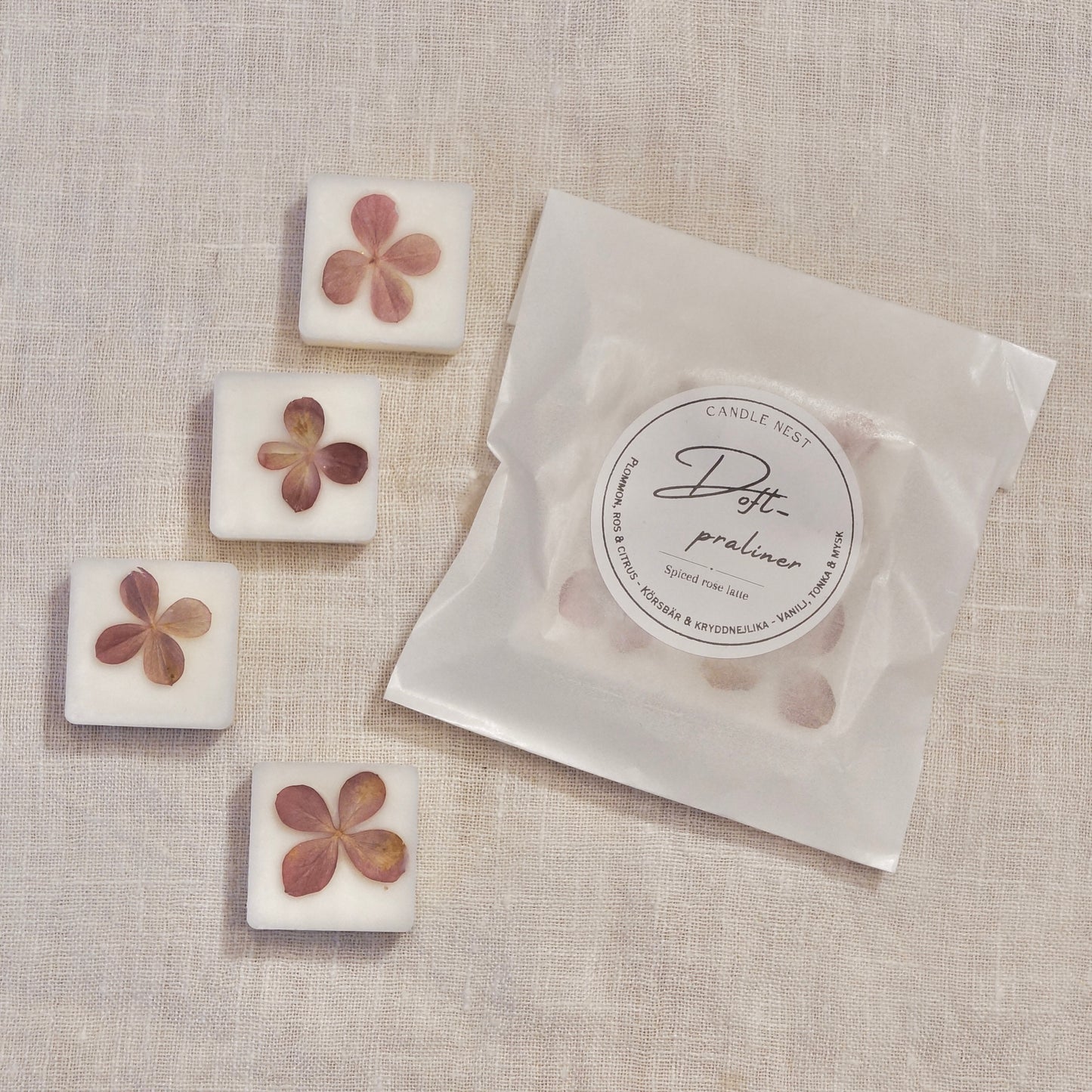 4 st doftpraliner i doften "Spiced rose latte" och en påse med doftpraliner ligger på en vit linneduk. Doftvaxen är dekorerade med torkad hortensia 