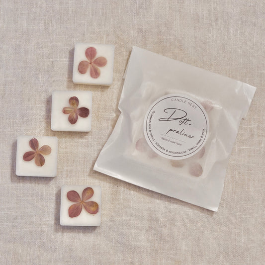 4 st doftpraliner i doften "Spiced rose latte" och en påse med doftpraliner ligger på en vit linneduk. Doftvaxen är dekorerade med torkad hortensia 
