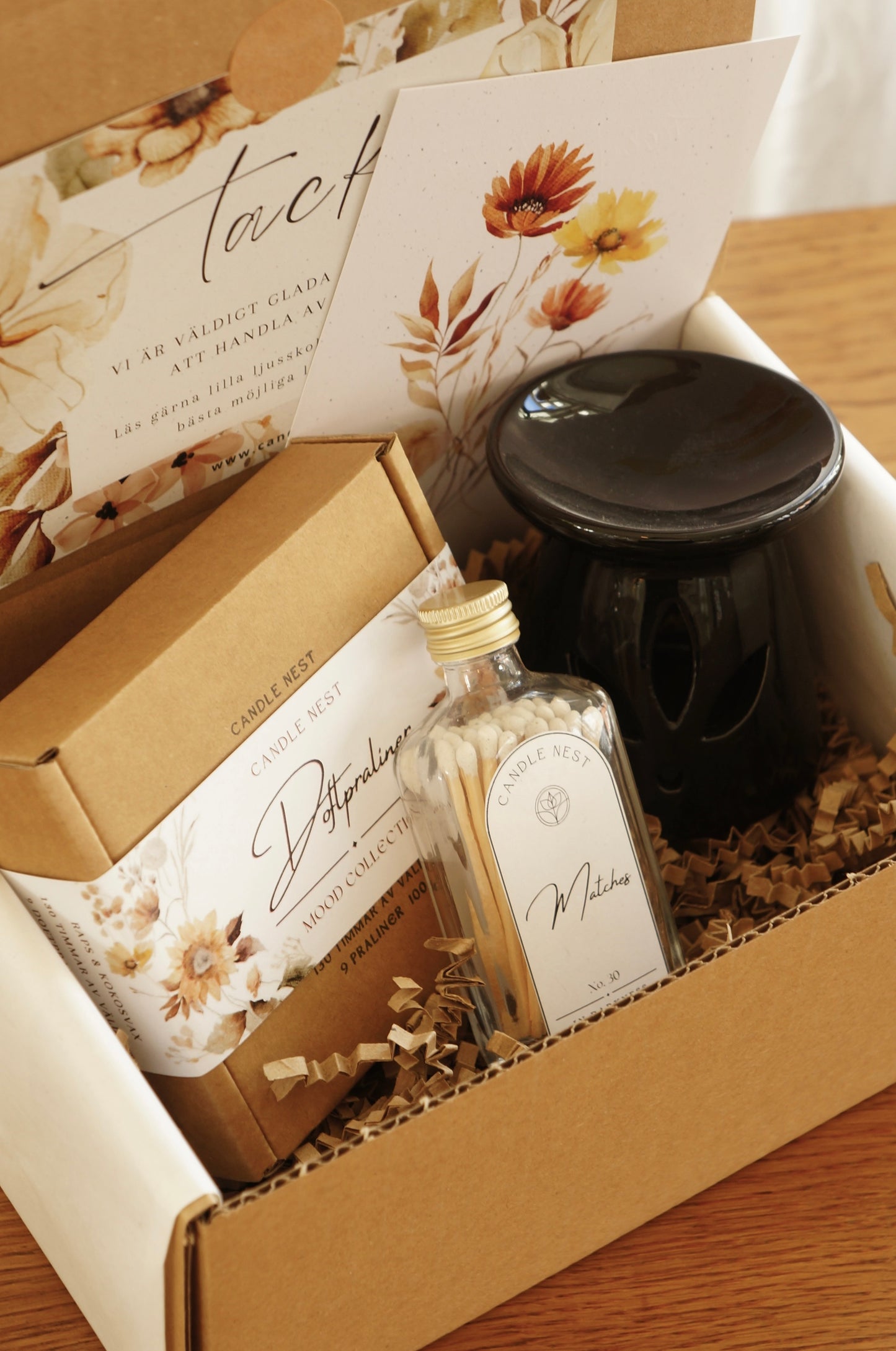Naturfärgad låda innehållandes en ask med Doftpraliner, en svart liten aromalampa och en flaska med tändstickor. 