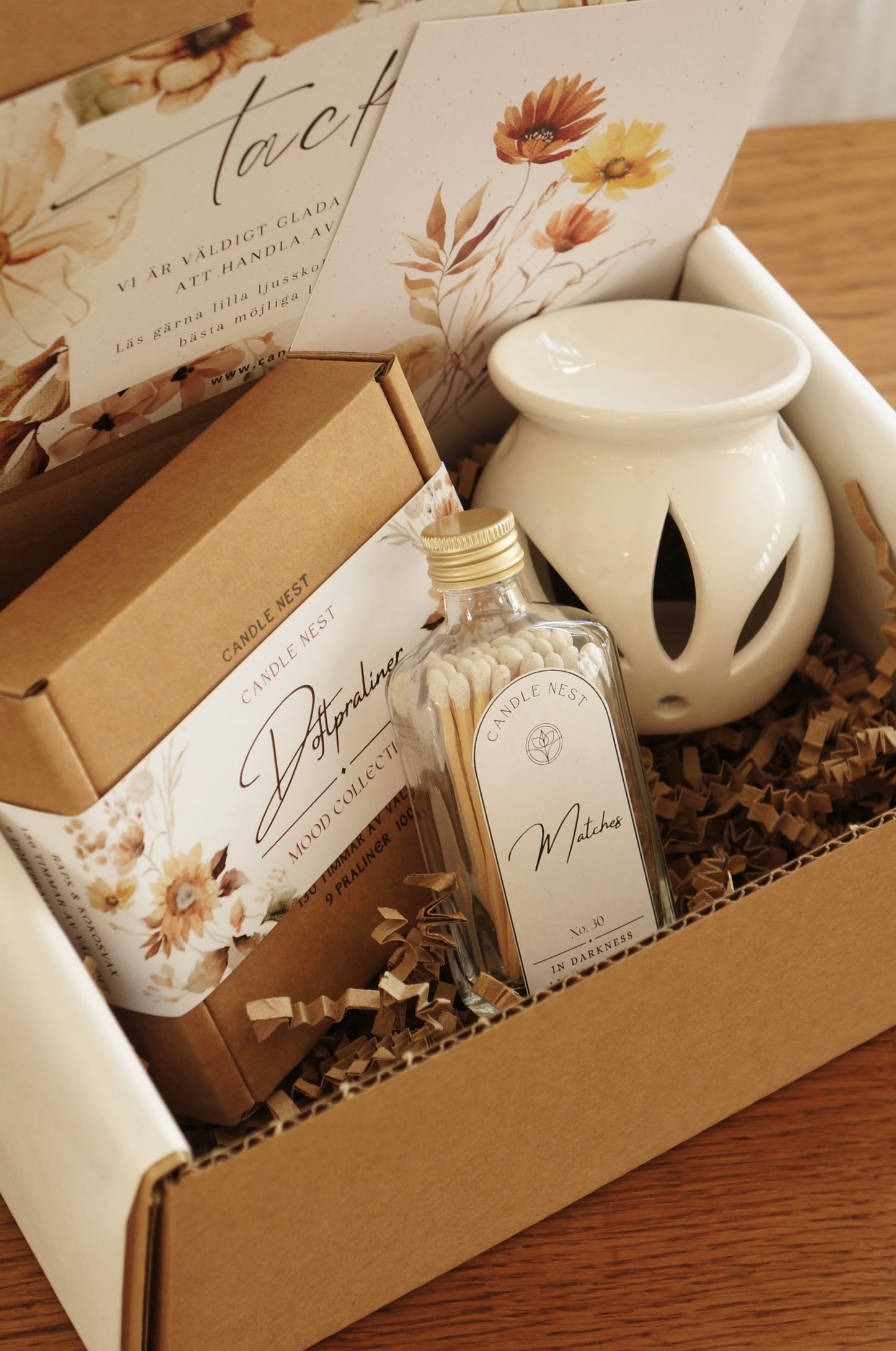 Naturfärgad låda innehållandes en ask med Doftpraliner, en vit liten aromalampa och en flaska med tändstickor. 