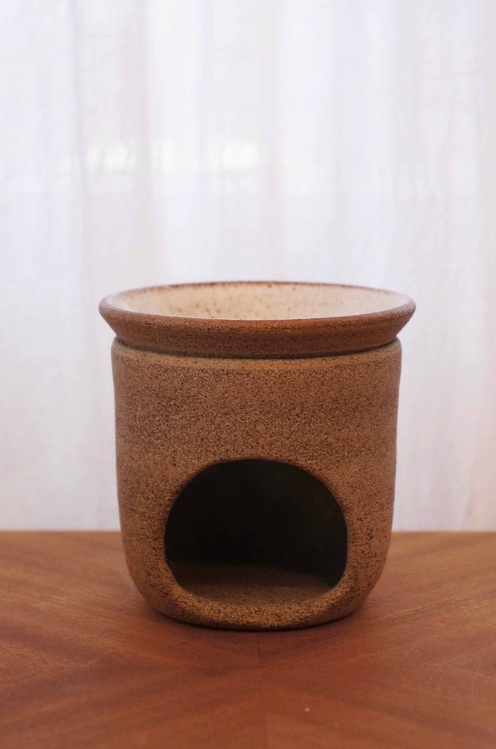 Handgjord aromalampa i keramik, visad från sidan med fokus på skålens runda öppning. Står på ett bord av trä framför en vit bakgrund.