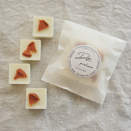 En Vit halvtransparent påse innehållandes fyra stycken doftpraliner ligger på en vit duk av linnetyg. Runt påsen ligger fyra stycken doft praliner dekorerade med en gran Grankvist