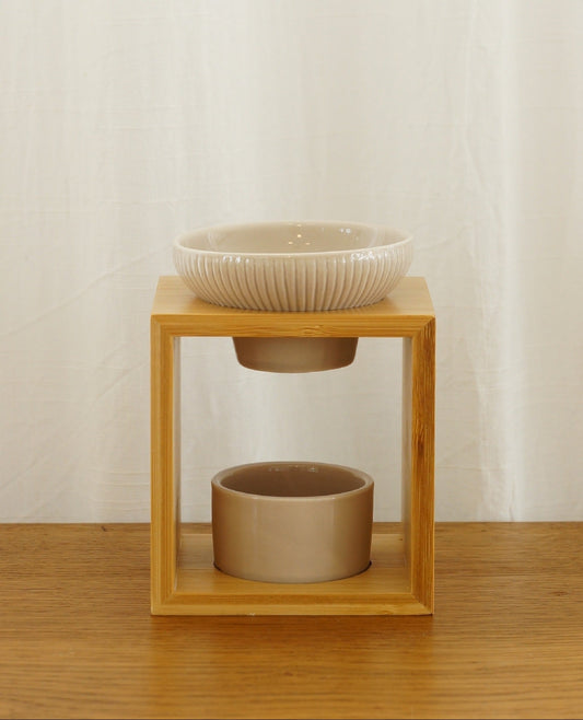 Modern och rustik aromalampa i beige keramik och bambu som står på ett bord av trä. Vit bakgrund.
