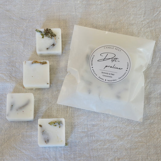Fyra vita doftpraliner med doften "Limoncello/ Serenity at Bali" dekorerade med tokad citronverbena . Doftvaxen är arrangerade på ett vitt linnetyg bredvid en transparent förpackningspåse från Candle Nest