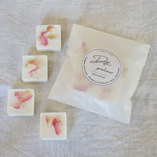 4 st doftpraliner i doften "Spiced rose latte" och en påse med doftpraliner ligger på en vit linneduk. Doftvaxen är dekorerade med rosa rosenblad och små runda glaspärlor