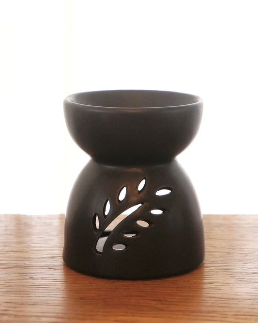 svart aromalampa i oval form står på ett bord av trä. På lampans framsida är det en öppning i form av en fjäder.