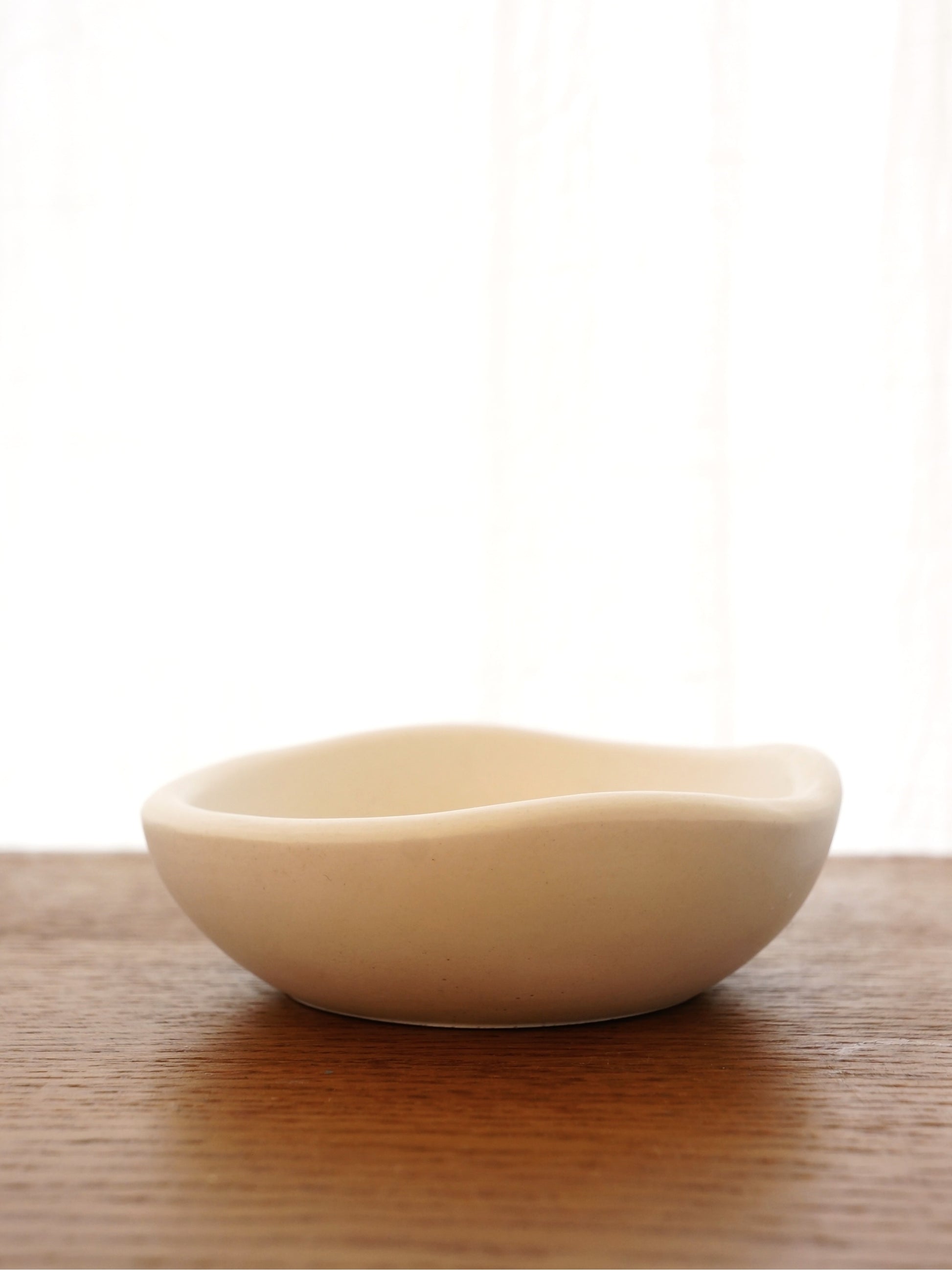 En liten vit skål i gips med vågformad kant står på ett mörkt bord av trä.