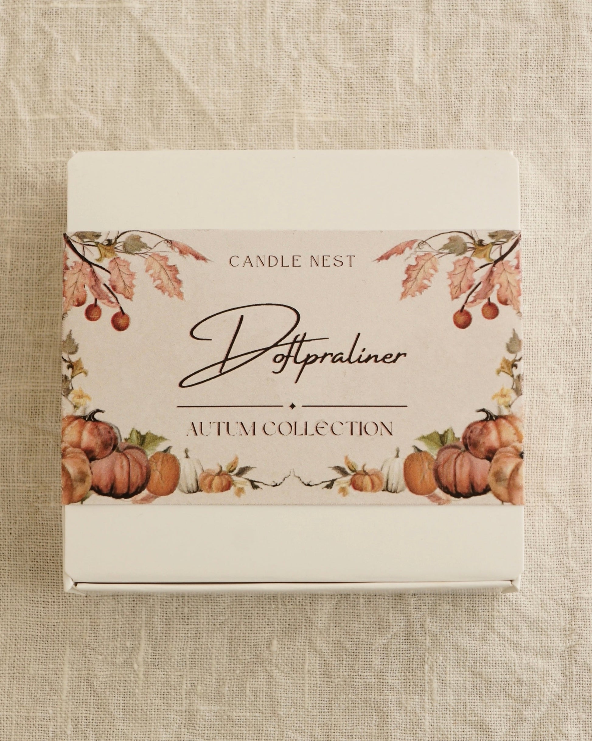 Candle nest ask med doftpraliner "Autumn collection" ligger på en vit linneduk. På asken syns bilder av pumpor och höstliga blad. Bilen är tagen uppifrån.