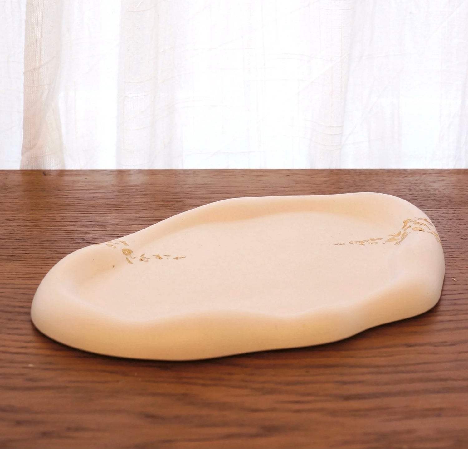 Molnformat vitt fat med dekor i guld ligger på ett bord av mörkt trä