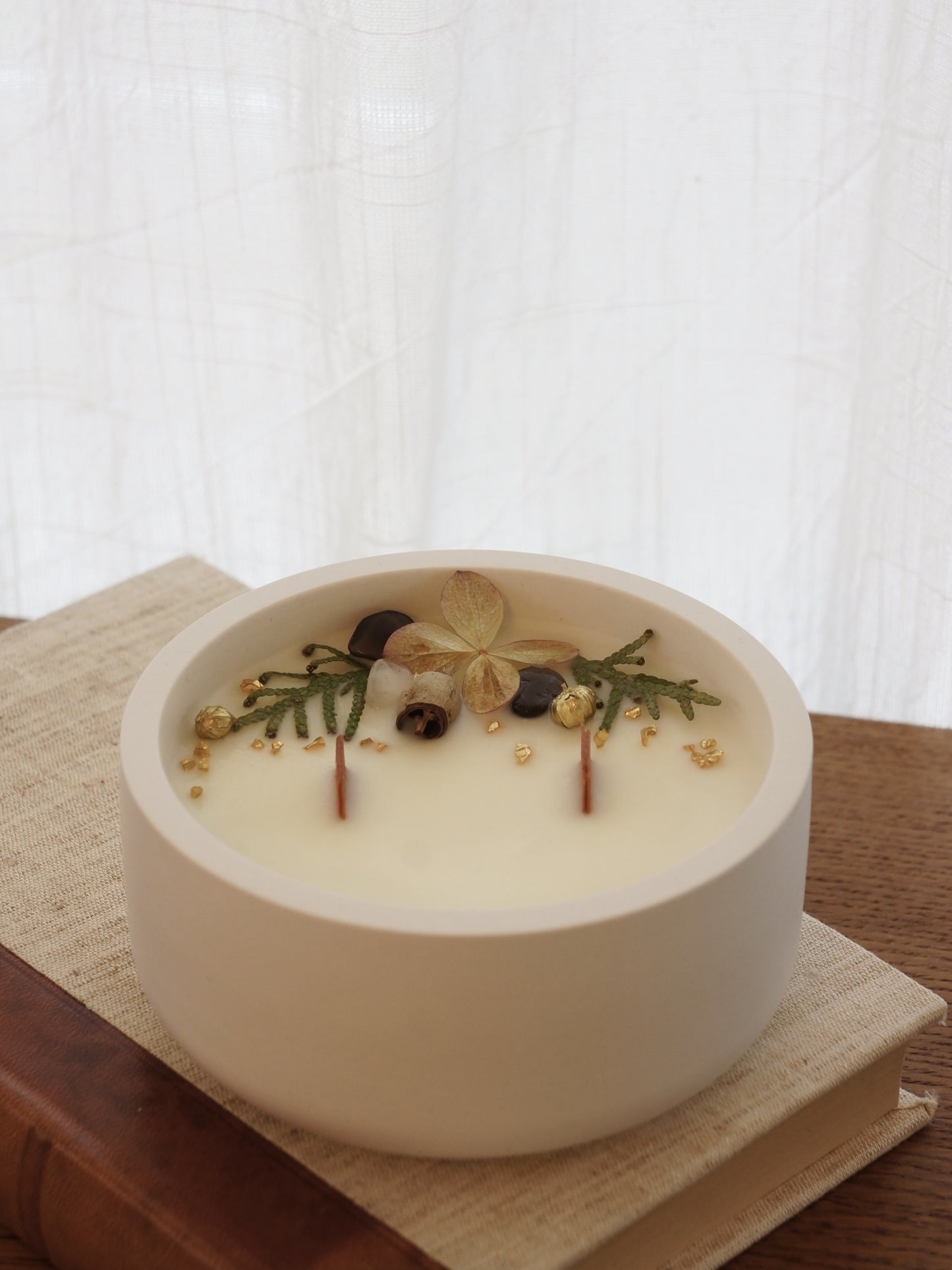 Handgjort doftljus i vit gipsskål med rapsvax, sprakande trävekar och mjuka, lyxiga dofter. Dekorerad med torkade blommor. Bild tagen snett uppifrån.