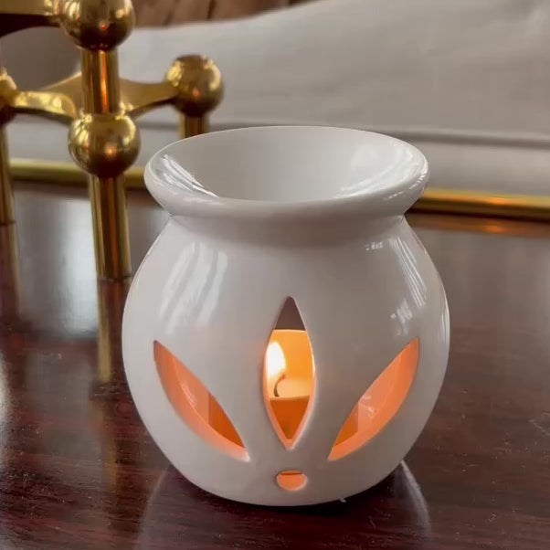 En liten vit aromalampa står på ett bord. En hand placerar en doftpralin i aromalampan. Man ser pralinen sakta smälta och blommorna som doftpralinen är dekorerad med frigöras